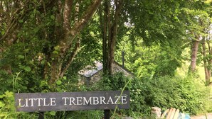 Een bord met de tekst 'Little Trembraze', omgeven door weelderige begroeiing en een stenen gebouw.