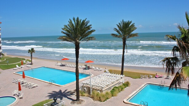 A resort with two swimming pools, beachside lounge chairs, and palm trees. - Enjoy your beach holiday in this updated oceanfront two bedroom, two bath condo. (New Smyrna Beach)