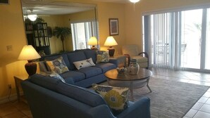 A living room with a blue sofa, two lamps, a coffee table, and a large mirror. - Enjoy your beach holiday in this updated oceanfront two bedroom, two bath condo. (New Smyrna Beach)