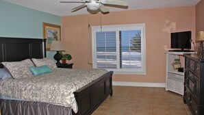 A bedroom with a bed, a ceiling fan, a window with blinds, a television, and a dresser. - Enjoy your beach holiday in this updated oceanfront two bedroom, two bath condo. (New Smyrna Beach)