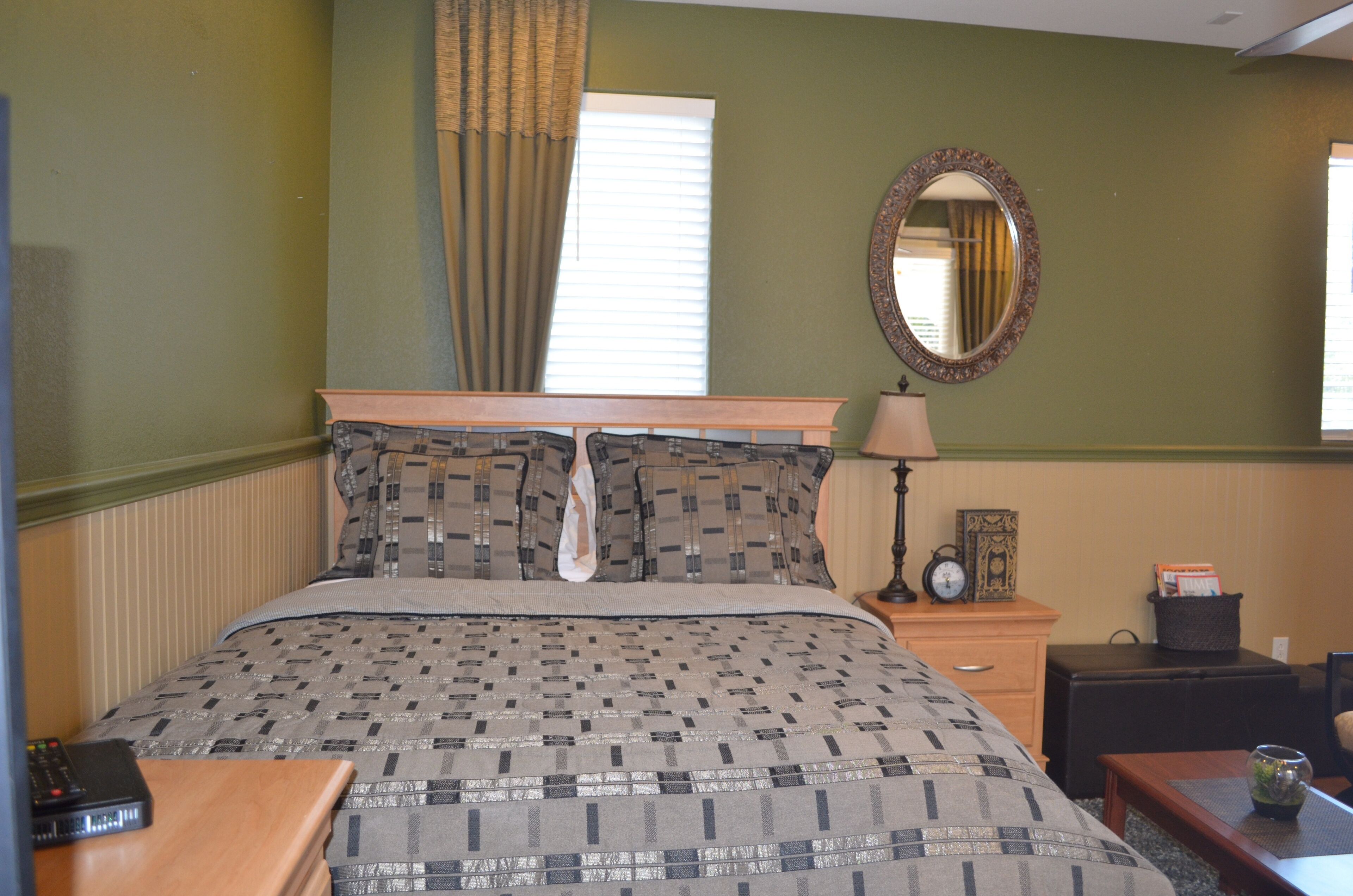 A neatly made bed with a patterned bedspread, a bedside lamp, a clock, and a small table with a cup.
