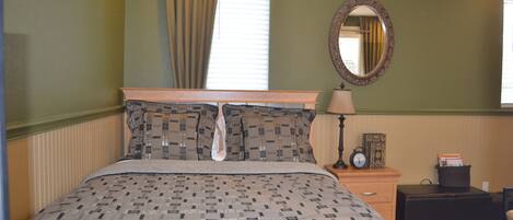 A neatly made bed with a patterned bedspread, a bedside lamp, a clock, and a small table with a cup.
