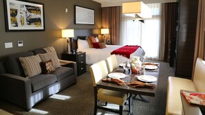 Una habitación de hotel con cama, sofá, mesa de comedor para dos personas y obras de arte en las paredes.