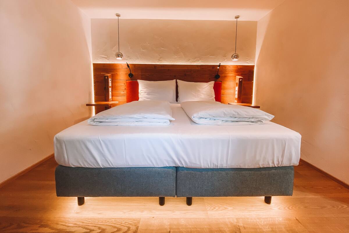 A neatly made bed with white linens, a wooden headboard, and a small bedside table with a lamp.