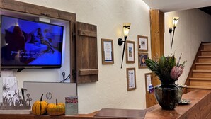 Un mostrador de recepción con detalles de madera, un televisor montado que muestra una imagen, diplomas enmarcados en la pared y una planta en maceta.