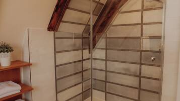 A modern bathroom with a glass shower enclosure, wooden shelves, and a potted plant.