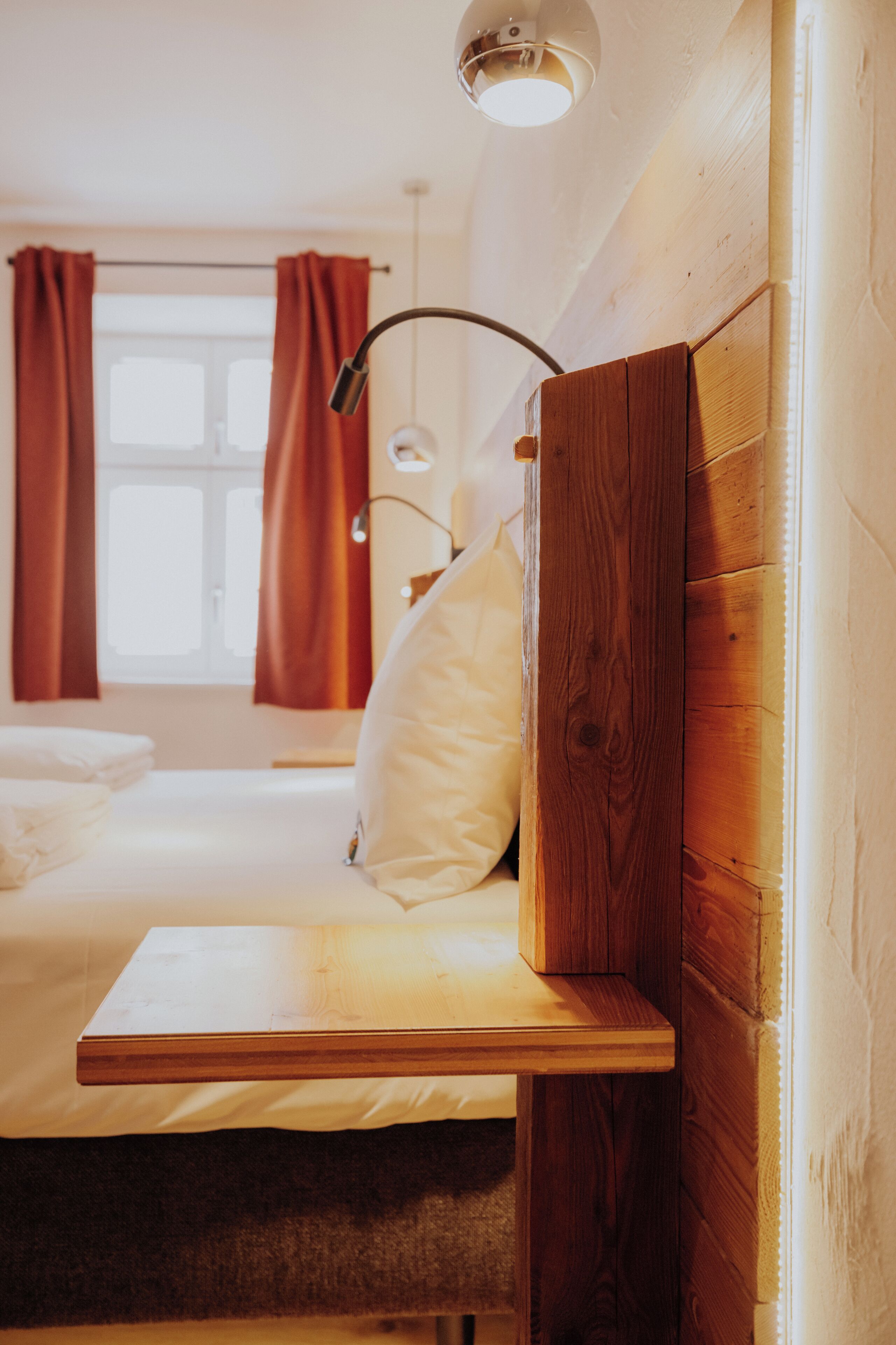 Een slaapkamer met een houten hoofdbord, een nachtkastje, een lamp en een raam met gordijnen.