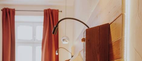 Un dormitorio con cabecera de madera, una mesita de noche, una lámpara y una ventana con cortinas.