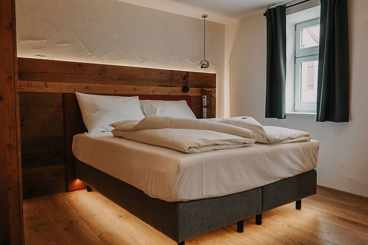A bed with a wooden headboard, a hanging light fixture, and a window with curtains.