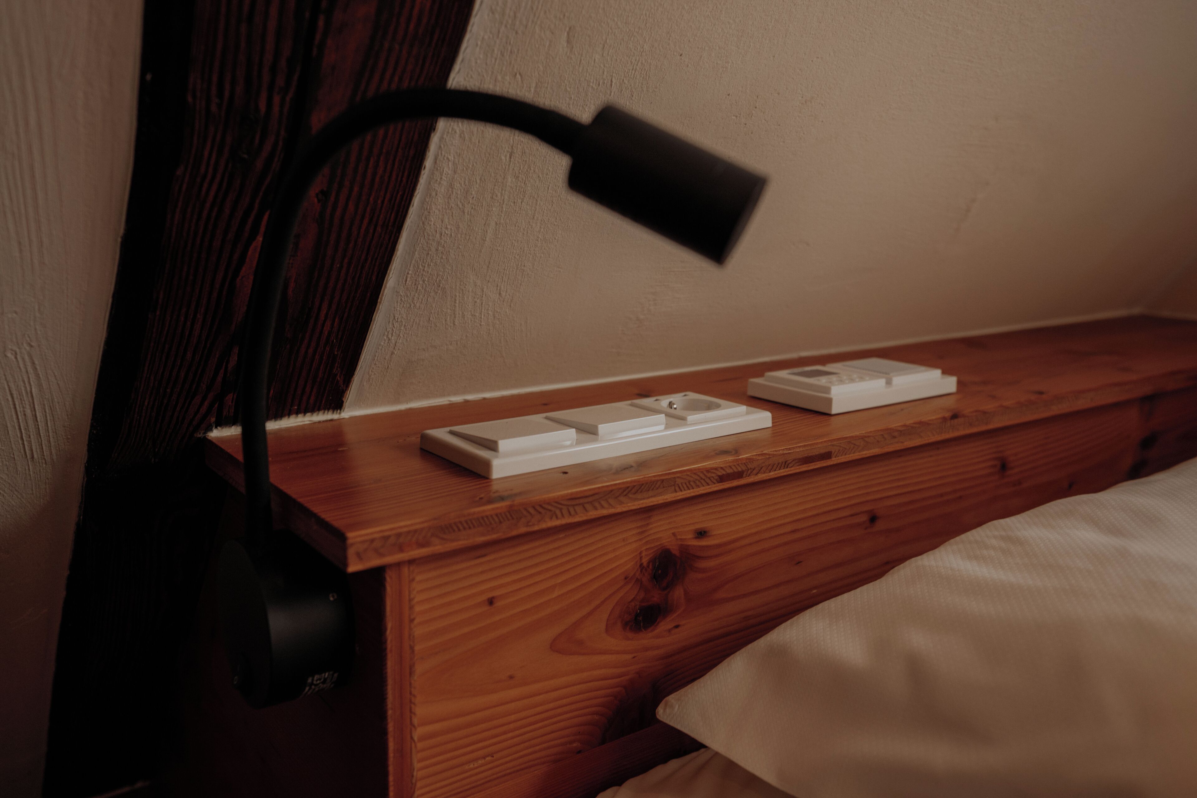 Una mesita de noche de madera con una lámpara de noche blanca y dos objetos blancos encima.