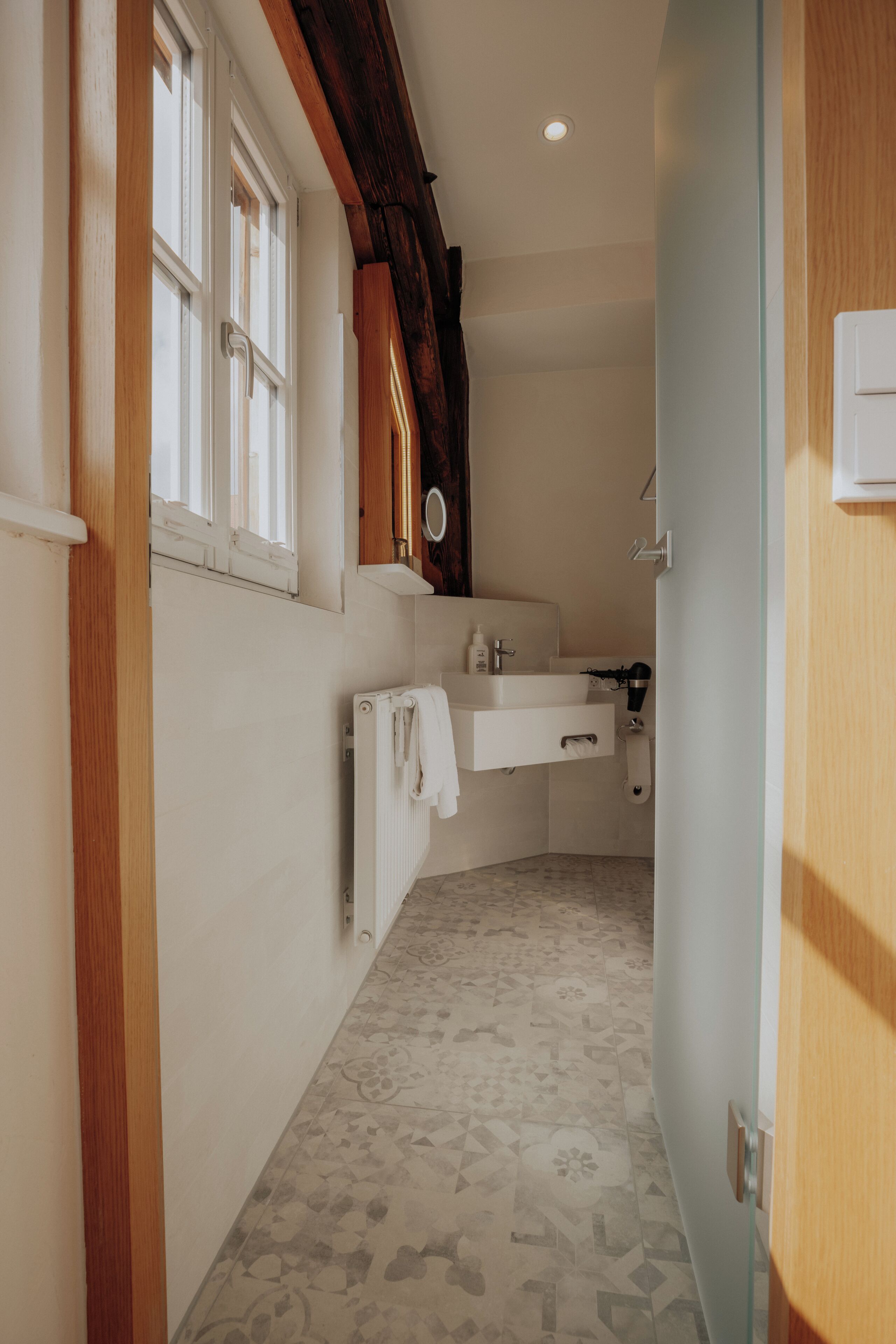 A narrow hallway with a bathroom on the right, featuring a sink, mirror, and towel rack.