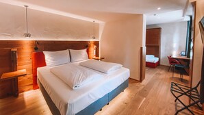 Un dormitorio moderno con cabecera de madera, cama con ropa de cama blanca, mesita de noche, escritorio con silla y armario.