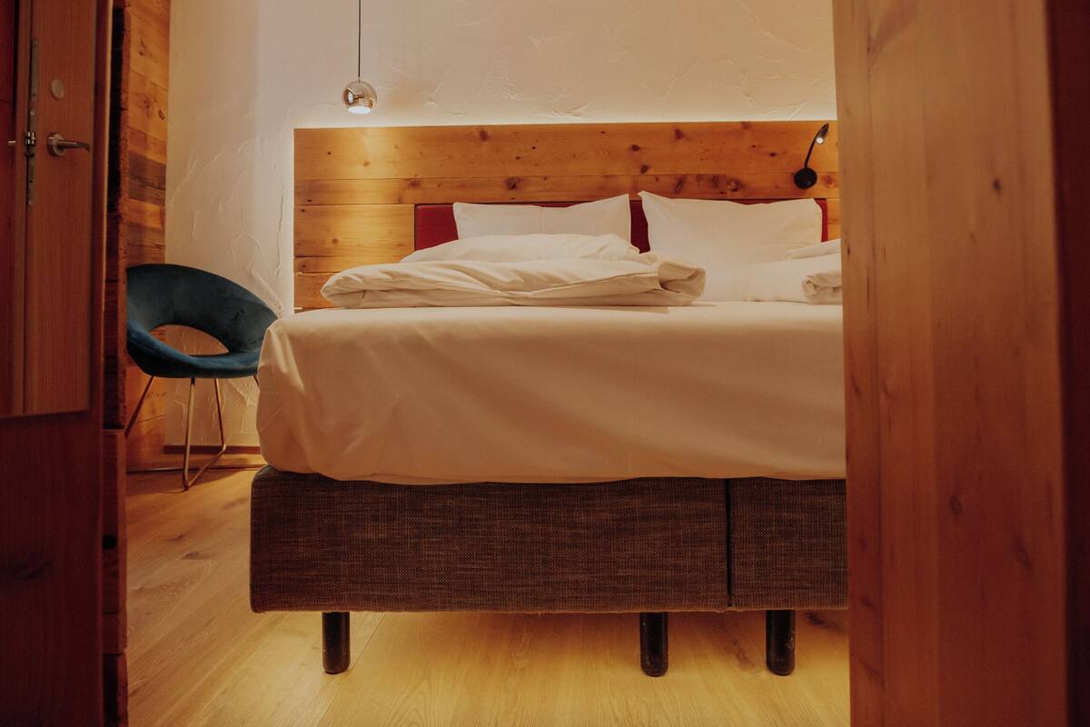 A bedroom with a wooden headboard, a bed with white linens, a blue chair, and a hanging light fixture.