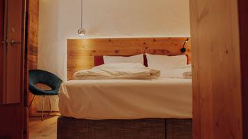 A bedroom with a wooden headboard, a bed with white linens, a blue chair, and a hanging light fixture.