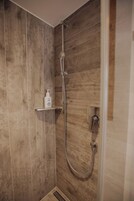Ducha con pared de madera, cabezal de ducha manual y una botella de champú en un estante.