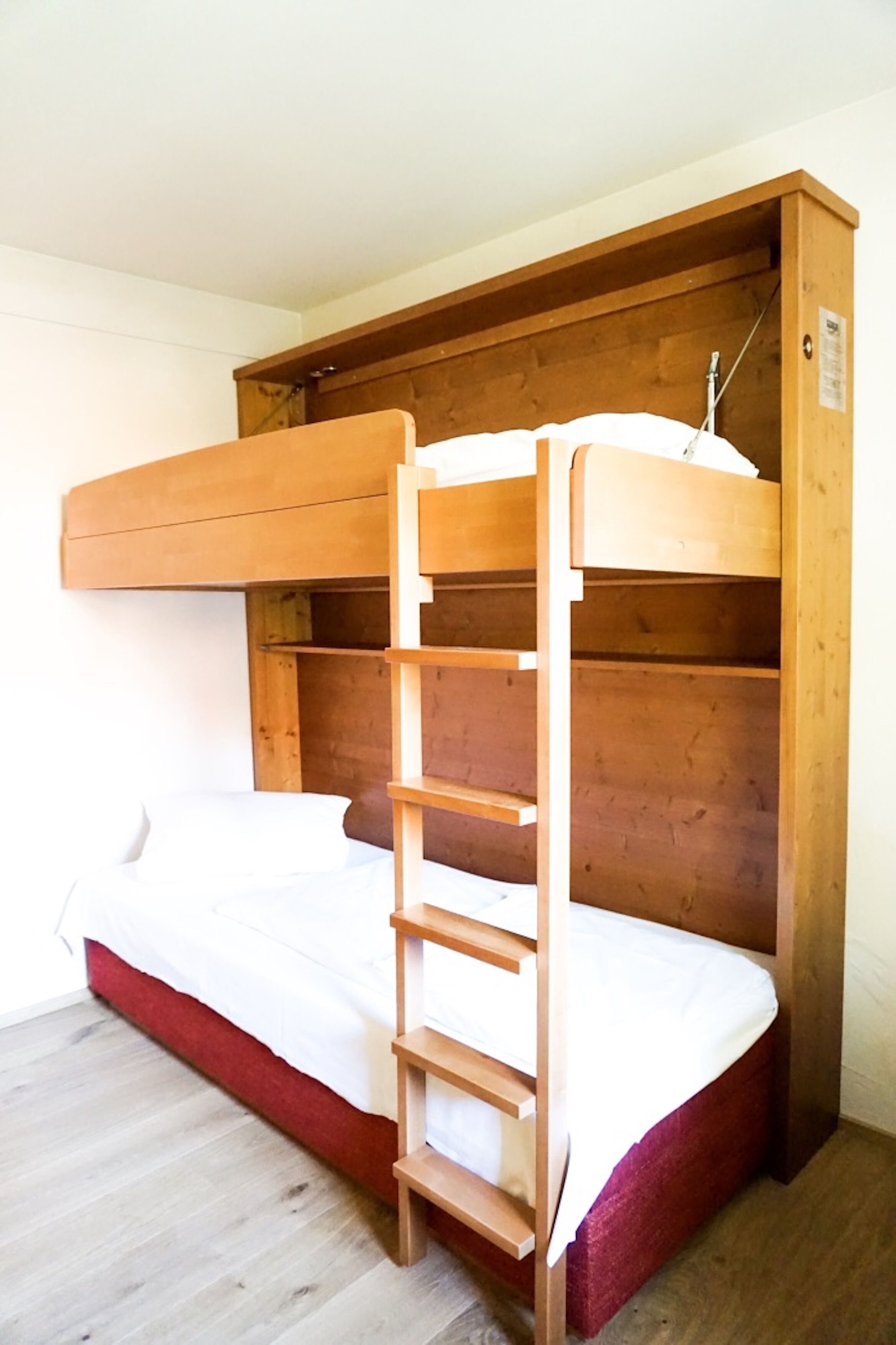 A bunk bed with a wooden ladder and a red mattress.