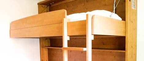 A bunk bed with a wooden ladder and a red mattress.