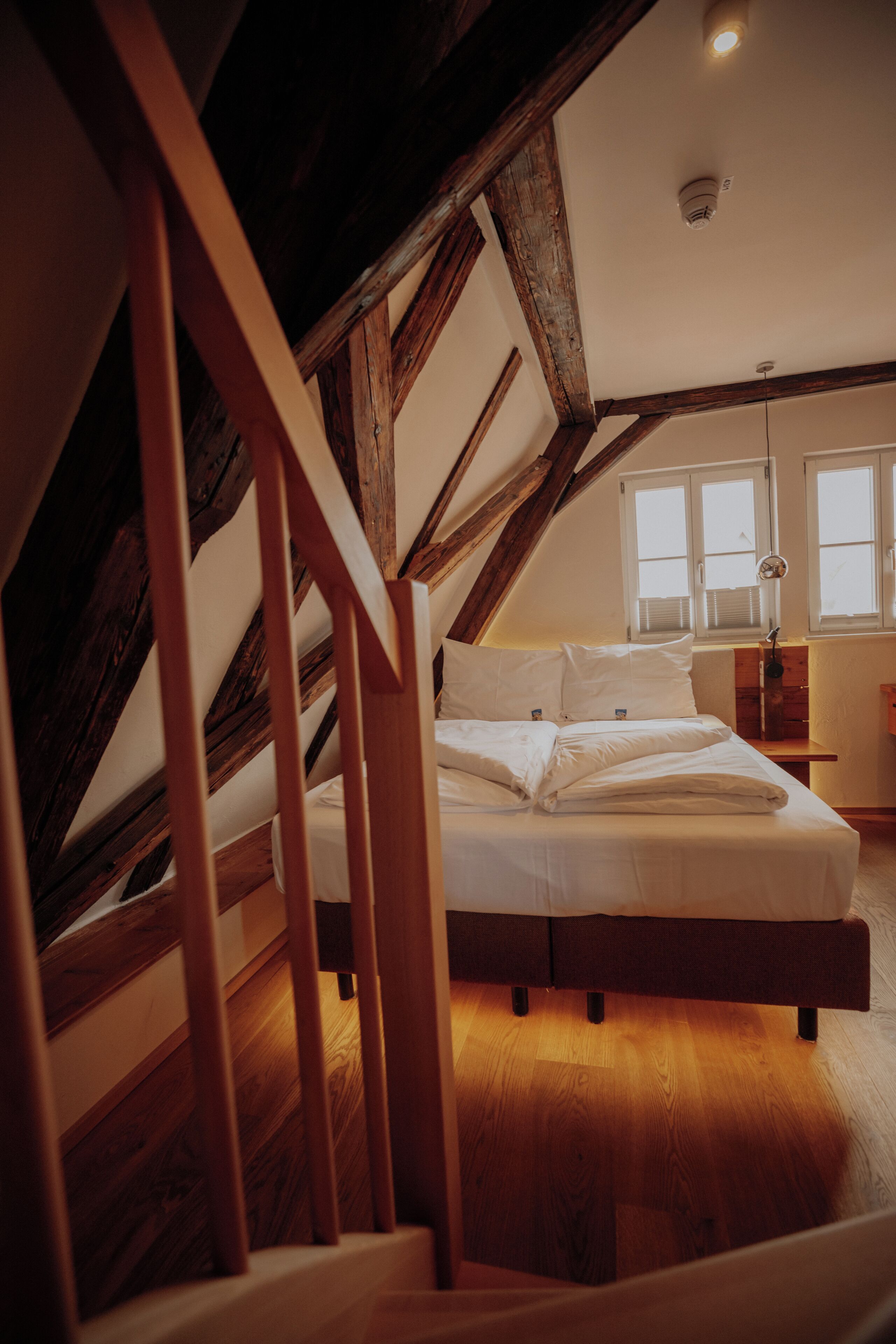 A bedroom with a wooden staircase, a bed, and a window with blinds.