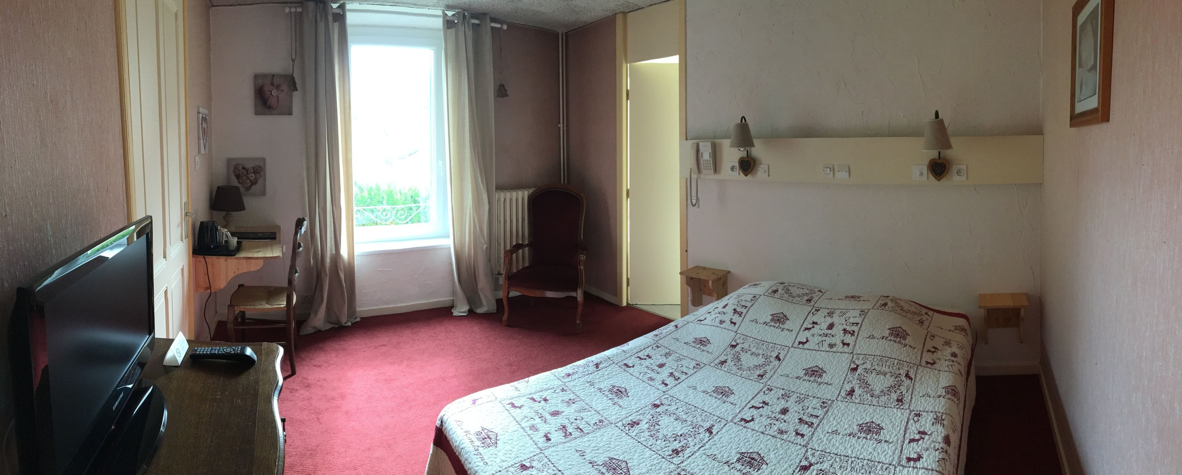 Habitación de hotel con cama, escritorio con computadora, una silla, televisor y ventana con cortinas.