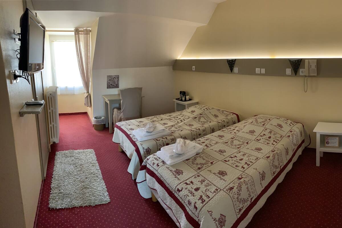 A hotel room with two beds, a TV, a small table with a coffee maker, and a radiator.