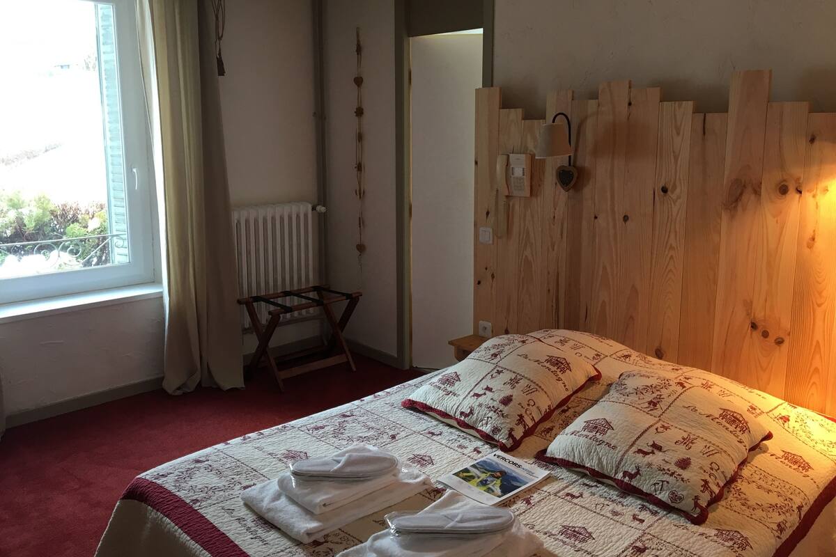 A bedroom with a wooden headboard, a bed with patterned bedding, a radiator, and a window with curtains.