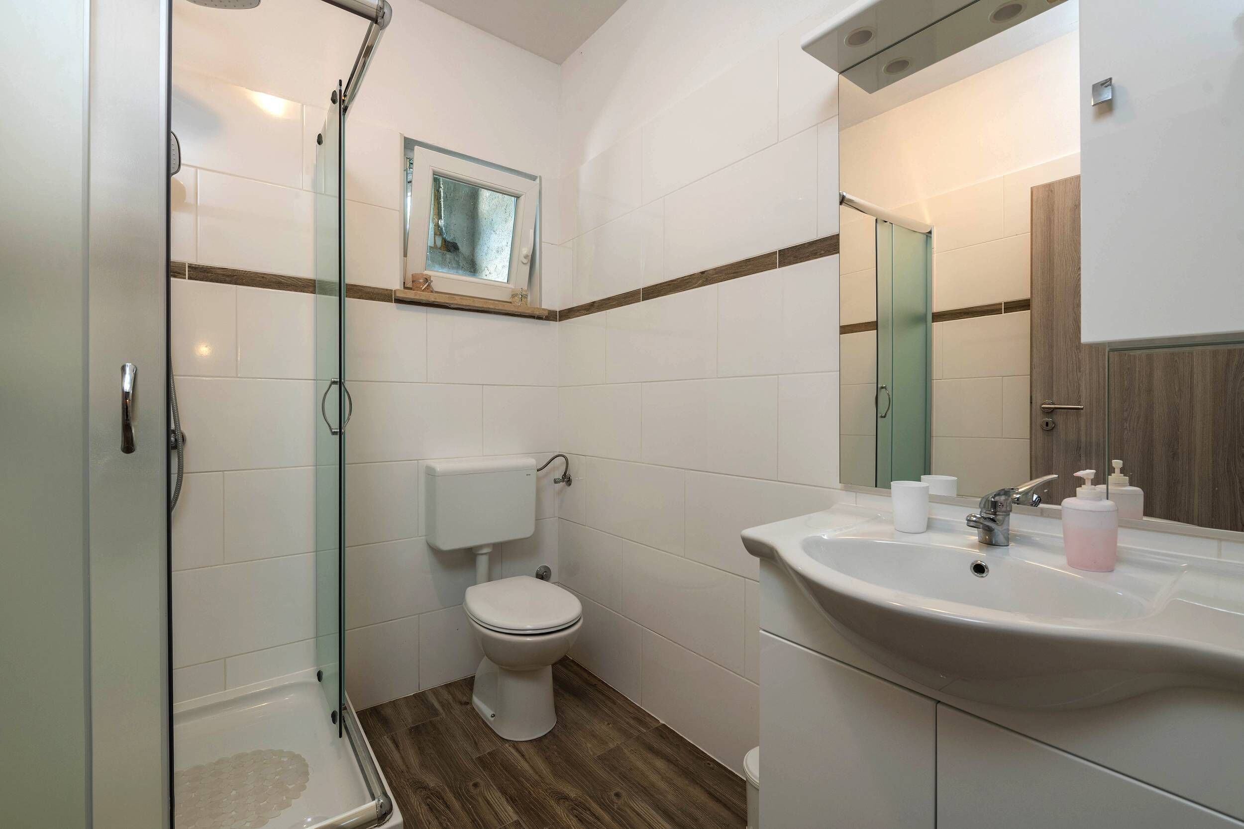 Un baño con cabina de ducha de vidrio, inodoro y lavabo con espejo.