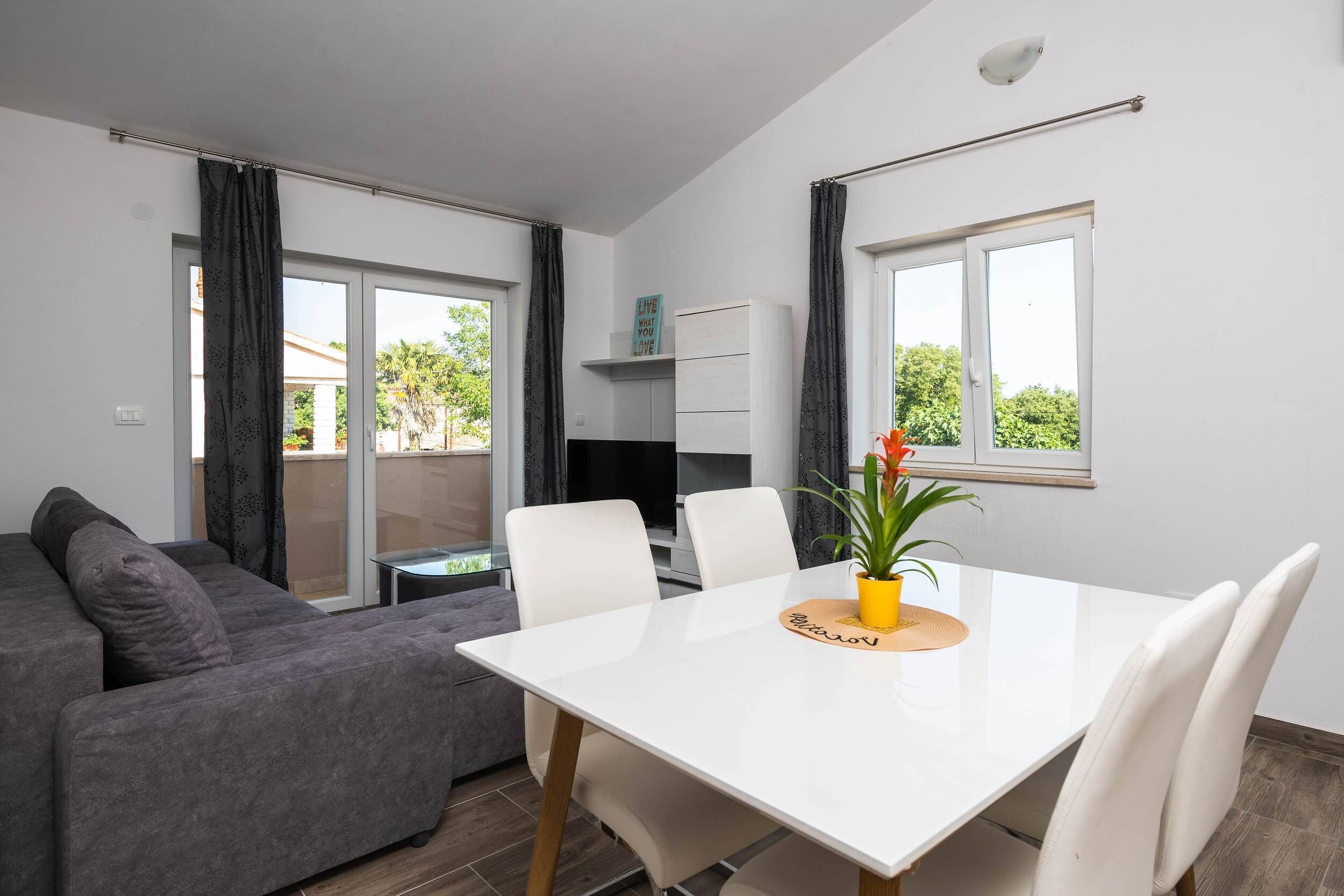 Una sala de estar moderna con una mesa de comedor blanca, un sofá gris y un televisor sobre un mueble.
