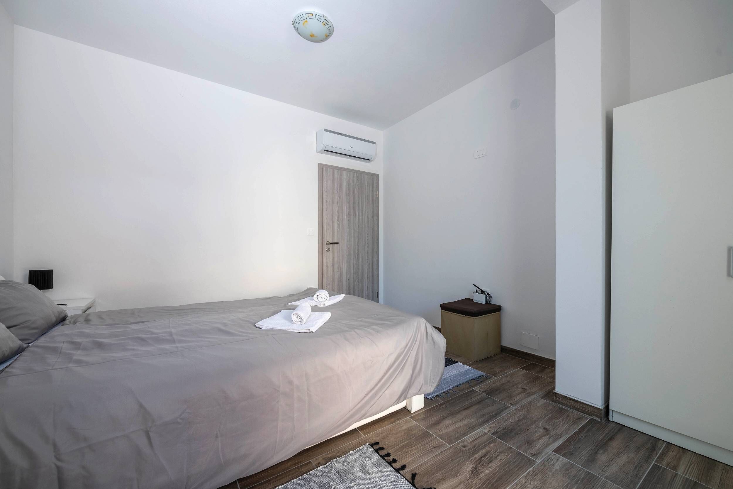 A modern bedroom with a bed, a nightstand, an air conditioning unit, and a wardrobe.