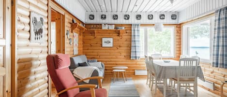 L’intérieur d’une cabane en rondins, avec un fauteuil rouge, un canapé, une table à manger et une vue sur l’extérieur.