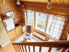 A wooden cabin interior with a kitchen, dining area, and a view of a lake.