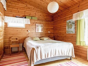 Een houten slaapkamer met een bed, bureau, stoel, hanglamp en raam met gordijnen.