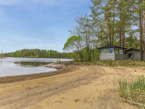 Un chalet au bord du lac, avec une plage de sable et une zone boisée en arrière-plan.