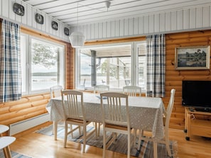 Een gezellig interieur van een chalet met een eettafel, stoelen, een televisie en uitzicht op een meer.