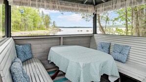 A covered outdoor seating area with a table and benches, overlooking a lake and forest. - Wuorilahti by Interhome (Savonlinna)