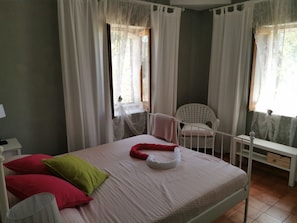 A bedroom with a bed, pillows, a chair, and a window with curtains. - Al passo di Talia (Ricadi)