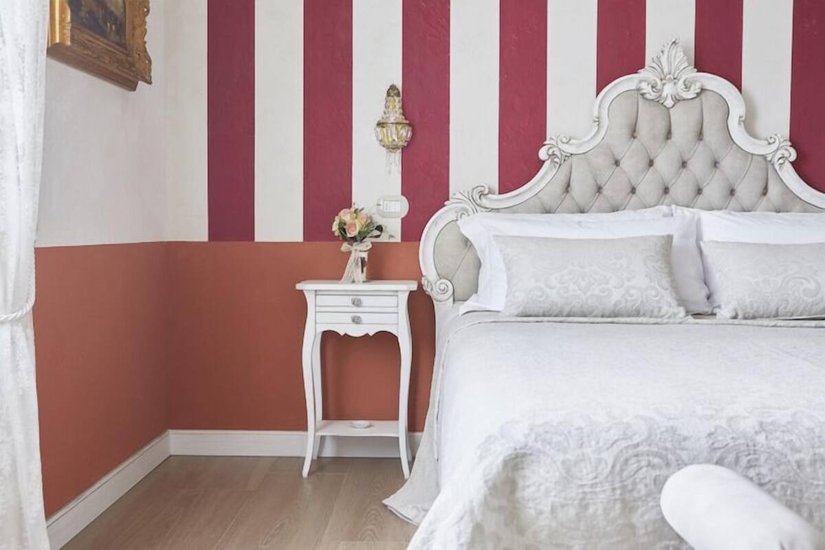 A bedroom with a white bed, a white nightstand, and a red and white striped wall.
