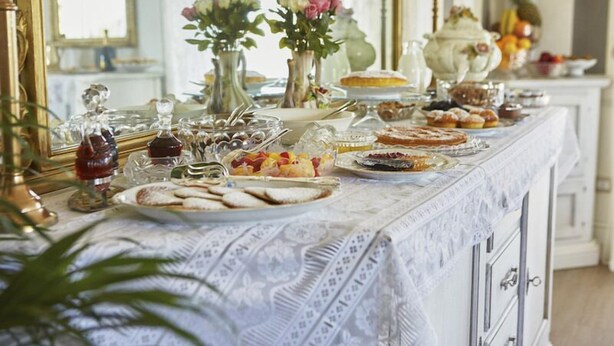 Una mesa de buffet con diversos platos y bebidas, ubicada en un salón con un espejo y jarrones decorativos.