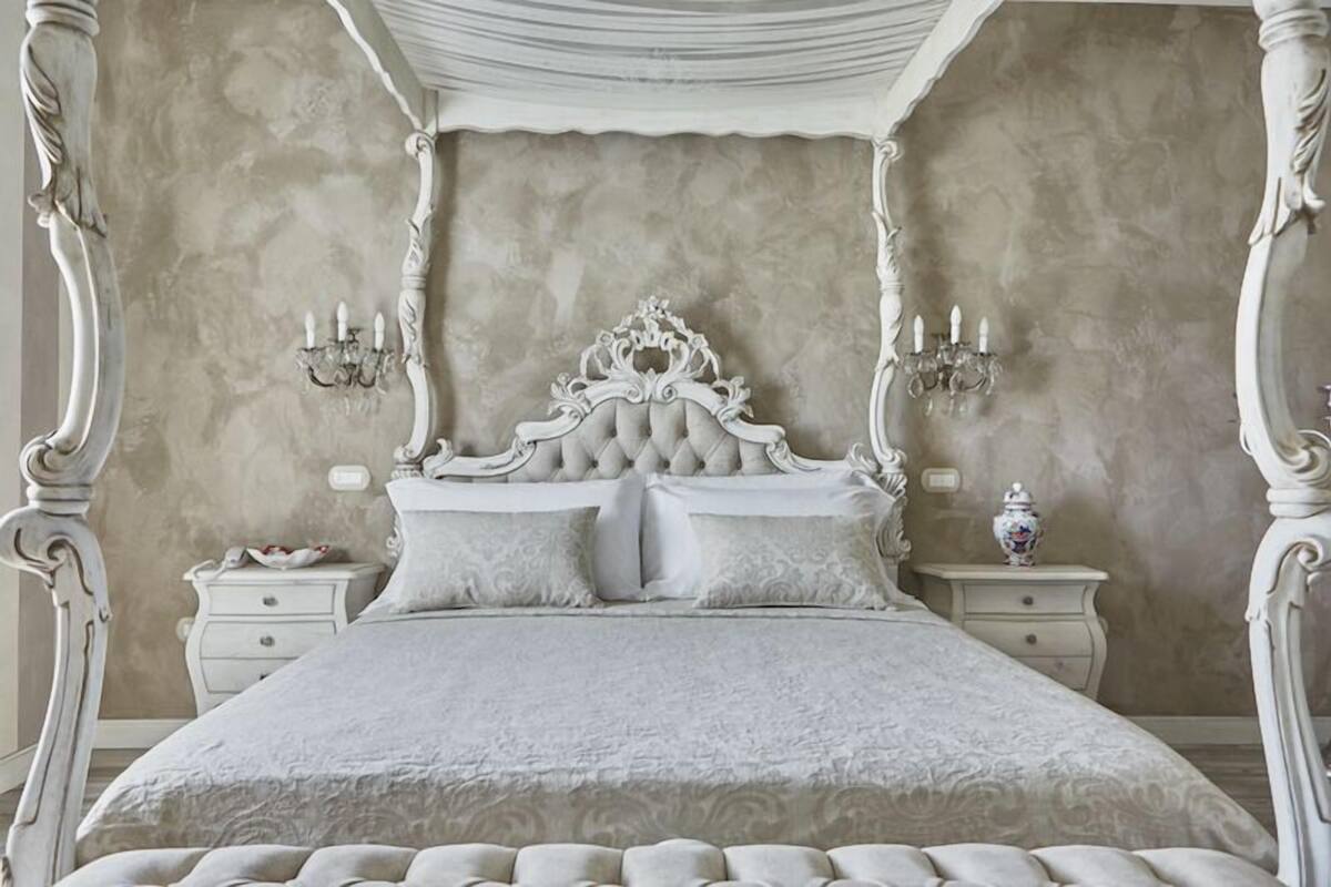 A four-poster bed with a tufted headboard, two bedside tables, and wall sconces.