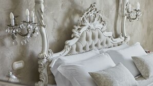Un dormitorio con un cabecero blanco ornamentado, una araña y un aplique de pared.