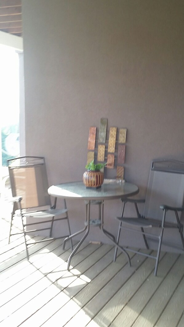 A patio area with a round table, two chairs, a potted plant, and a wall with wooden panels. - Enjoy relaxing sounds of our Creek 2 (Penn Valley)