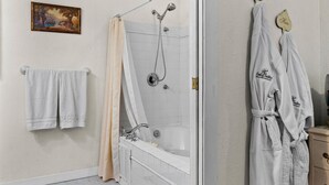 Un baño con bañera, ducha, toallas y un cuadro en la pared.