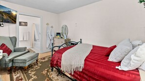 Un dormitorio con cama, una silla, cómoda, espejo y puerta.
