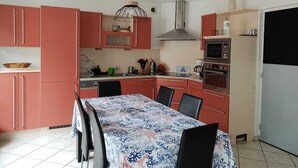 Une cuisine de taille réduite avec des placards roses, une table à manger avec des chaises, un four à micro-ondes et une cuisinière.