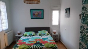 Une chambre à coucher comprenant un lit, deux tables de chevet, une lampe suspendue, une fenêtre avec des rideaux et une porte.