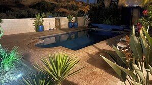 A swimming pool with a tiled deck, surrounded by potted plants and a white wall. - VILLA LES PALMIERS /300M2/15 PERS/PISCINE/7 CH/6 SDB/GARAGE/EXCEPTIONAL VIEWS (Aourir)