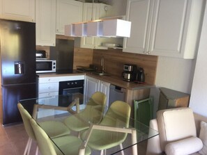 Una cucina moderna con mobili bianchi, un frigorifero nero, un forno a microonde e una macchina da caffè. C'è un tavolo da pranzo in vetro con due sedie.