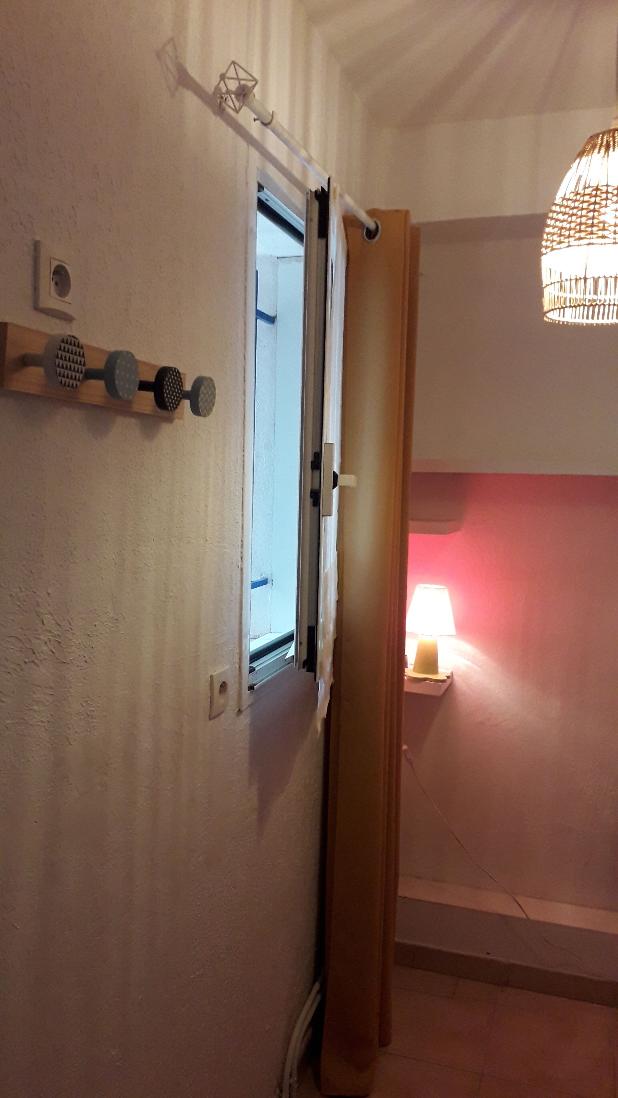 Une pièce avec une porte en bois, une fenêtre avec des stores, un luminaire fixé au mur et une lampe suspendue.