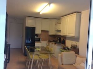 Una cucina compatta con mobili bianchi, un frigorifero nero, un tavolo da pranzo in vetro con sedie gialle e una poltrona beige.