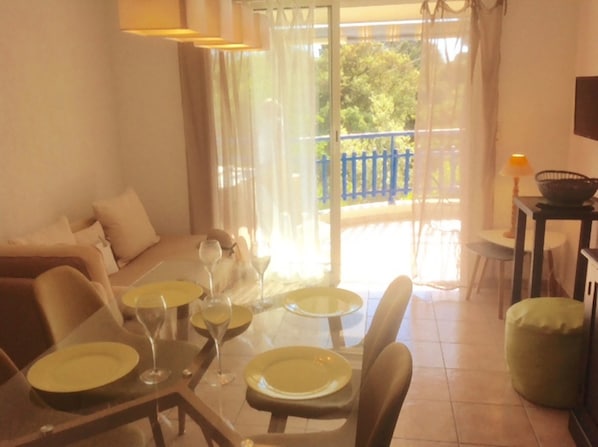 Zona pranzo con tavolo apparecchiato per quattro, divano e balcone con ringhiera blu.