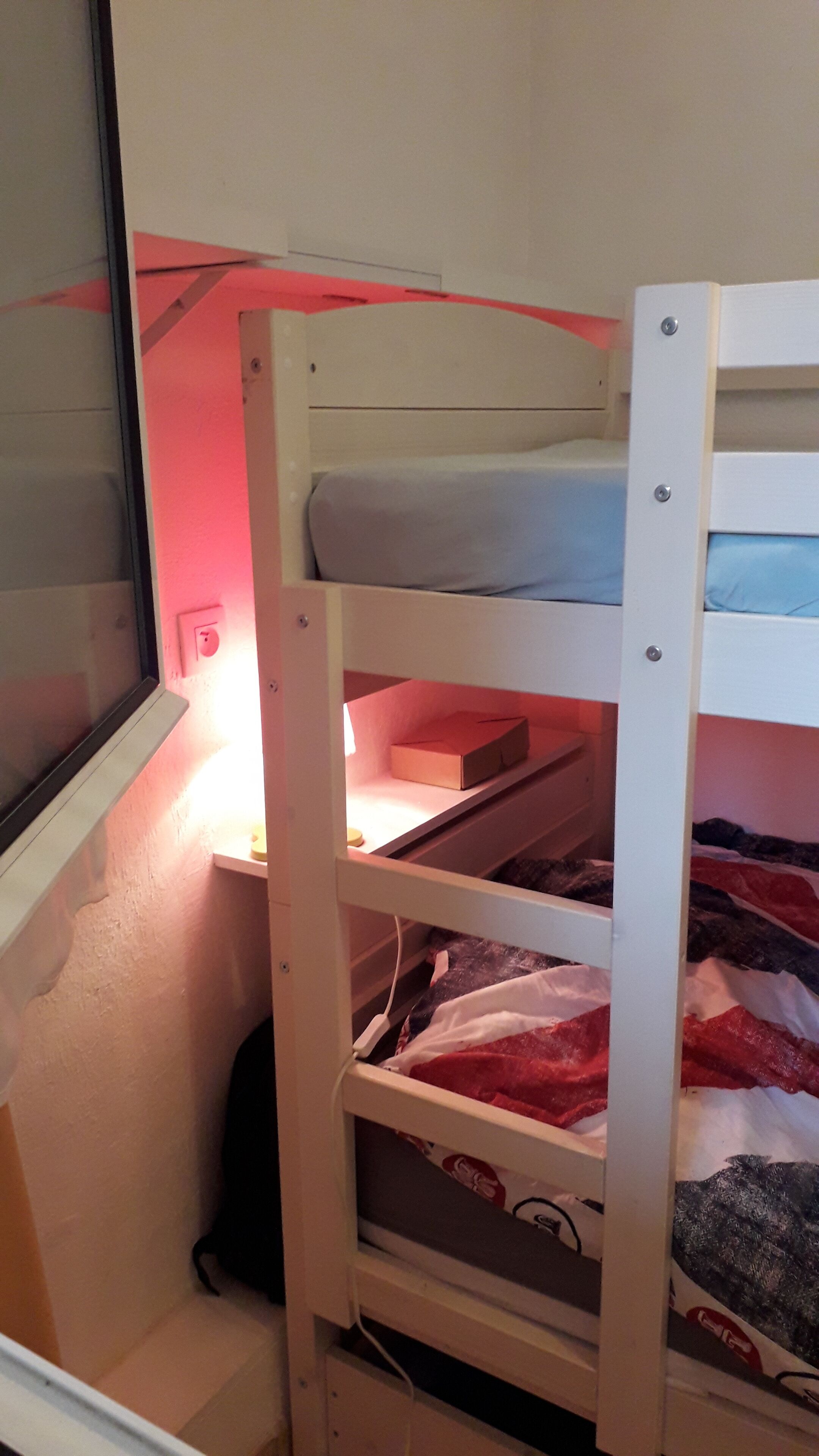 A bunk bed with a shelf underneath and a window to the left.